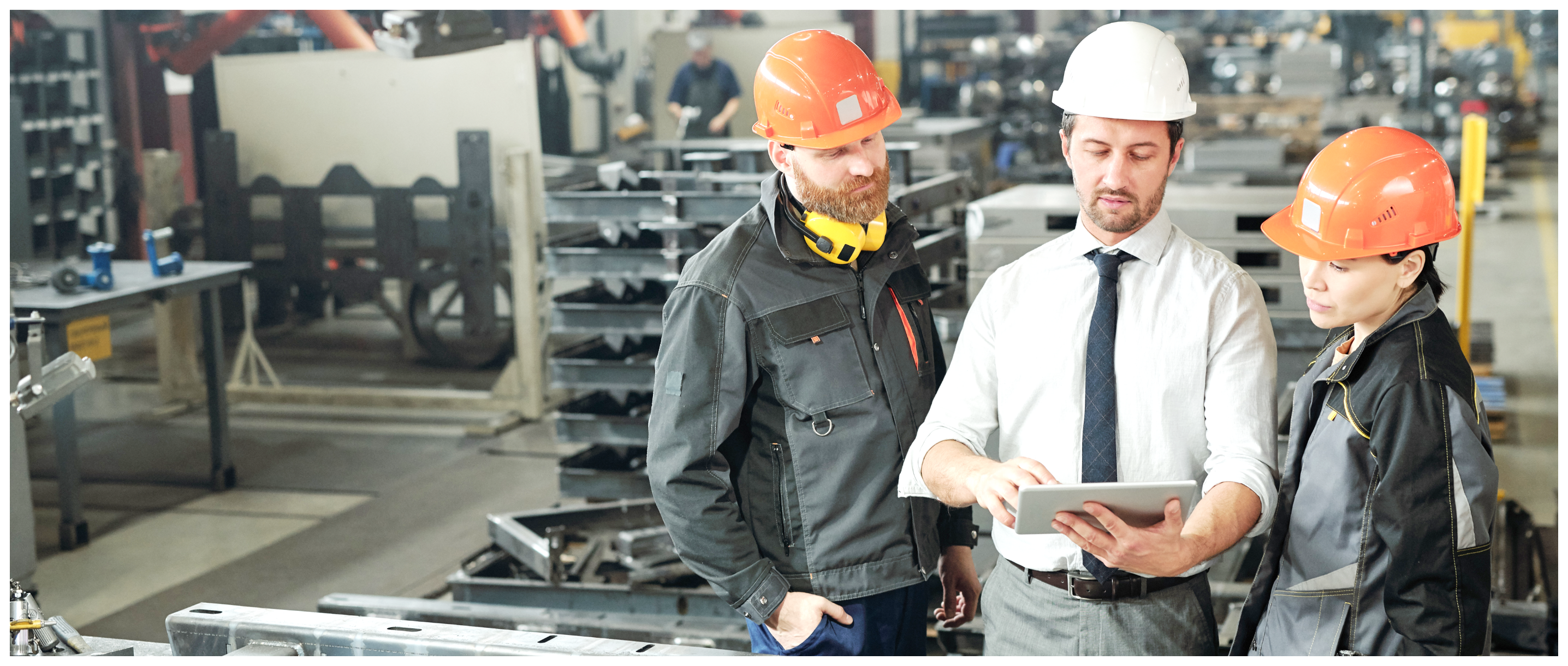 Using a digital tablet and helmets, a warehouse team discusses one another.